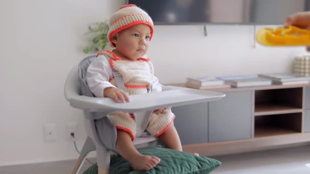 Sandalyesinde oturan bir bebek kahvaltıda yemeğini evde yer. Bebek sütten kesme konsepti - Video, Çekim