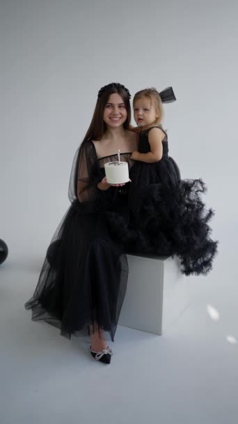 Een mooie jonge moeder in een feestelijke jurk houdt een verjaardagstaart vast voor haar dochtertje. - Video