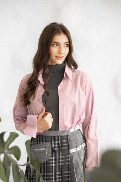 портрет молодой улыбающейся женщины в модной одежде с розовой курткой, позирующей у стены. - Фото, изображение