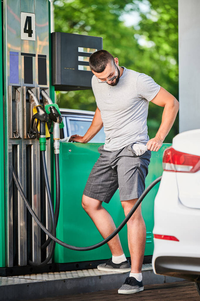 Man left without money after spending all on fuel. Guy showing his empty pockets after refueling his car. Transportation expenses concept. - Photo, Image
