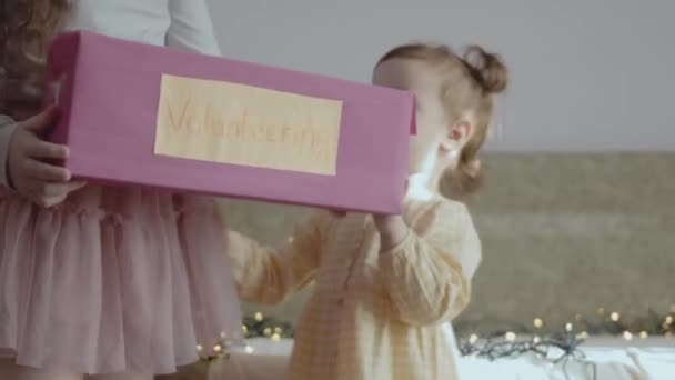 Klein meisje geeft een liefdadigheidsdoos die ze heeft gemaakt aan een peuter meisje. Kerstvrijwilligerswerk - Video
