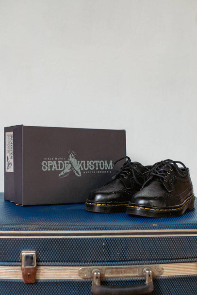 Klasyczne czarne skrzydełka brogue buty wykonane z oryginalnej skóry, wyświetlane na czarnym pudełku po butach i zużytej walizce vintage. Koncepcja zdjęcie vintage buty z klasycznym stylu - Zdjęcie, obraz