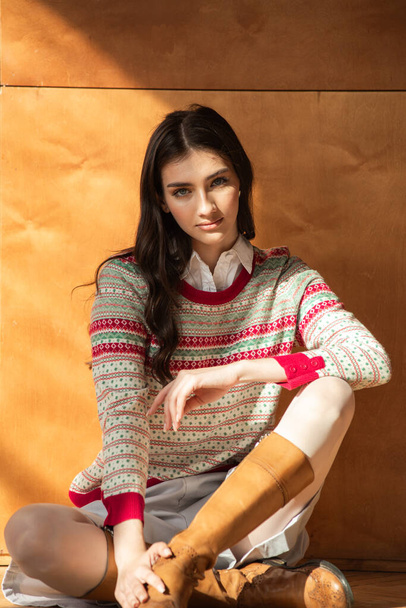 красивая девушка в свитере и носках сидит на деревянном столе и смотрит в камеру - Фото, изображение