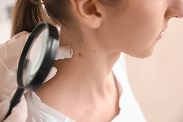 Dermatólogo examinando lunar en el cuello de la mujer joven con lupa en la clínica, primer plano - Foto, Imagen