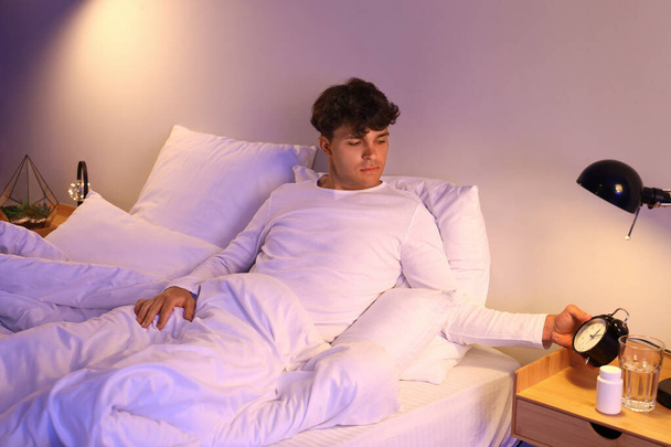 Jongeman kijkt 's nachts naar de tijd in bed - Foto, afbeelding