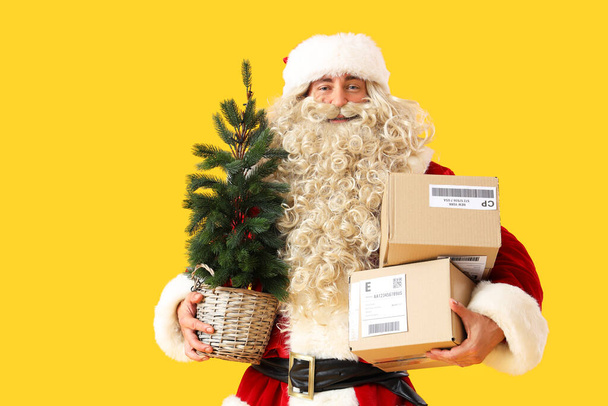 Санта-Клаус с елкой и посылками на желтом фоне - Фото, изображение