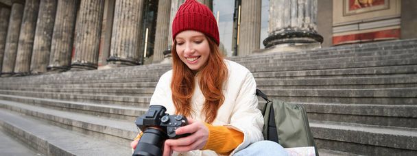 Молода студентка, фотограф сидить на вуличних сходах і перевіряє свої кадри на професійній камері, фотографуючи на відкритому повітрі
. - Фото, зображення