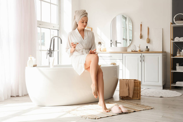 Junge Frau cremt sich nach Dusche im Badezimmer das Bein ein - Foto, Bild