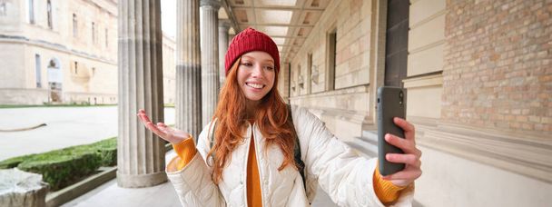 Happy girl tourist demonstrates something on video chat smartphone, shows sightseeing attraction to friend while on mobile phone app call. - Zdjęcie, obraz