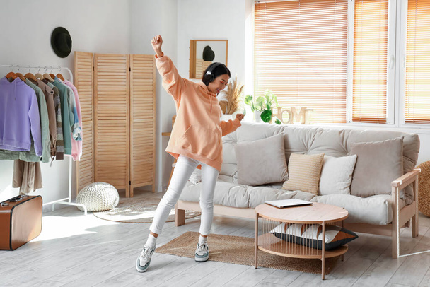 Young Asian woman in stylish hoodie with headphones dancing at home - Foto, Imagem