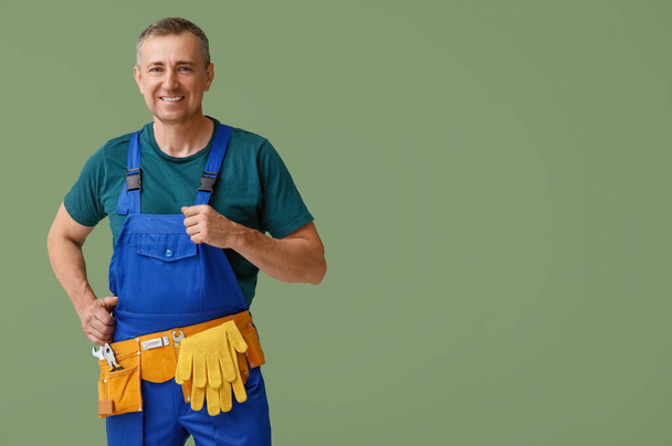 Портрет мужчины-механика с инструментальным поясом на зеленом фоне - Фото, изображение