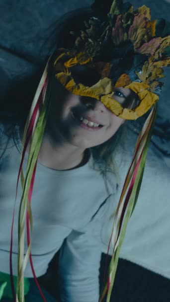 Portret van een klein meisje dat een herfstbladmasker afdoet en een kerstmuts opzet, poserend en glimlachend naar de camera. Overgang van herfst naar winter concept. Verticaal, handheld schieten. - Video