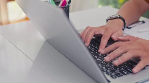 Close-up van handen van onherkenbare man met behulp van laptop en het maken van notities tijdens het studeren van thuis - Video