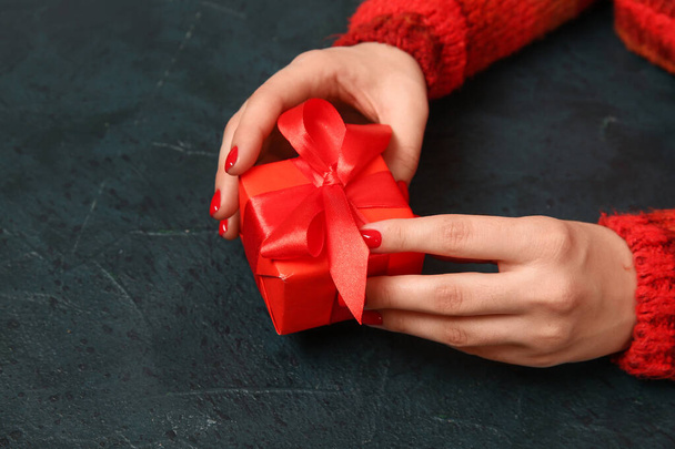 Жіночі руки з червоним манікюром та різдвяною подарунковою коробкою на чорному гранжевому фоні - Фото, зображення