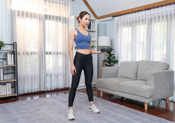 自宅でダンベル体重を持ち上げるエネルギッシュな女性. 若い運動アジアの女性の強さと耐久トレーニングセッションホームワークアウトルーチンとして. - 写真・画像