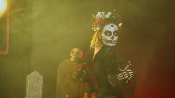 Donna affascinante con teschio di zucchero trucco e fascia fiori, vestito in costume dea della morte come Santa Muerte. Dios de los muertos arte per celebrare la tradizione messicana in studio. Colpo palmare. - Foto, immagini