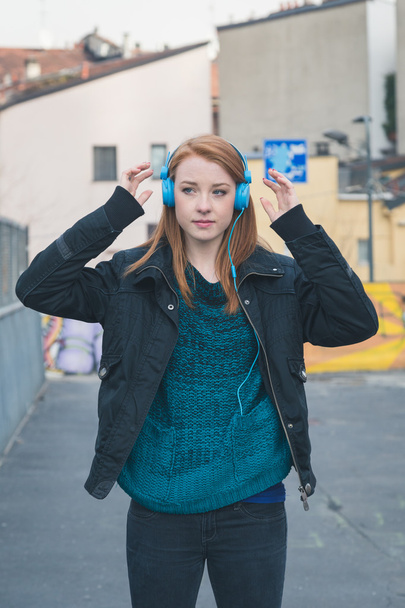 Όμορφη κοπέλα με τα ακουστικά που θέτουν στους δρόμους της πόλης - Φωτογραφία, εικόνα