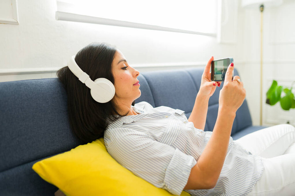 Jeune femme détendue regardant une vidéo en streaming sur son téléphone en utilisant et app pour apprendre et étudier l'anglais en ligne à la maison - Photo, image