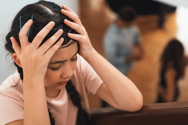 Gestresste und unglückliche junge Mädchen verdecken ihre Ohren und blockieren die Geräuschspannung durch das Argument ihrer Eltern von der Treppe aus. Ungesunde familiäre und häusliche Gewalt führen zu traumatischen Kindheits- und Angstzuständen. Synchronos - Foto, Bild