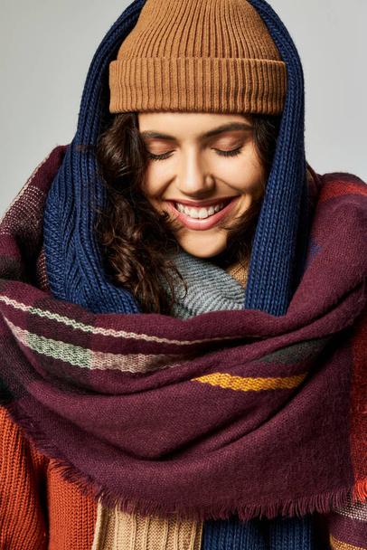 Kış modası, katmanlı giysiler içinde neşeli bir kadın, gri arka planda örülü şapka ve eşarplar. - Fotoğraf, Görsel
