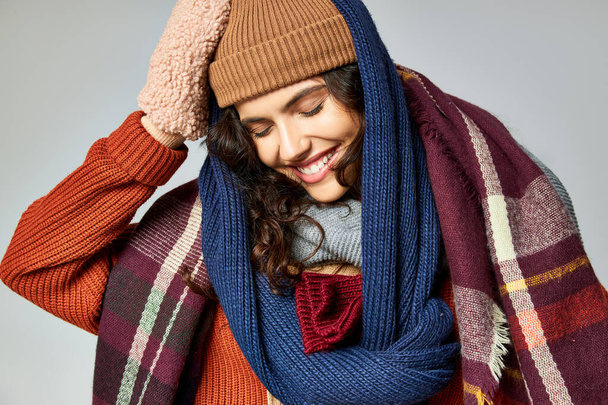 moda invernale, donna allegra in abiti a strati, cappello caldo e sciarpe in posa su sfondo grigio - Foto, immagini