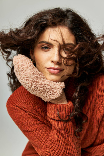 wind blowing at face of curly brunette woman in terracotta sweater and mittens, winter fashion - Photo, Image