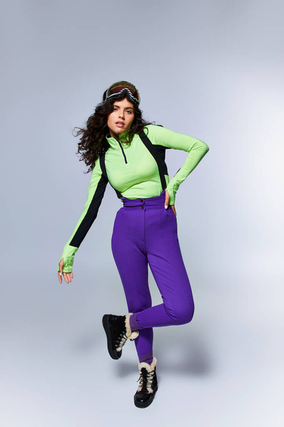 winter sport, full length of sporty woman with curly hair posing in active wear on grey backdrop - Photo, Image