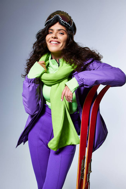 winter activity, smiling woman with curly hair posing in active wear with puffer jacket and skis - Photo, Image