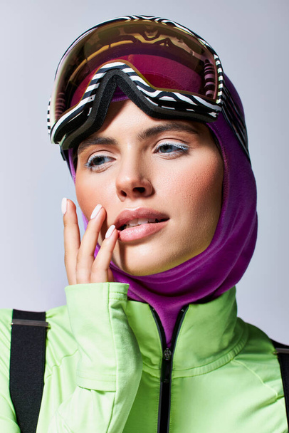 belle femme en hiver vêtements de ski avec cagoule sur la tête posant avec la main près du visage sur gris - Photo, image
