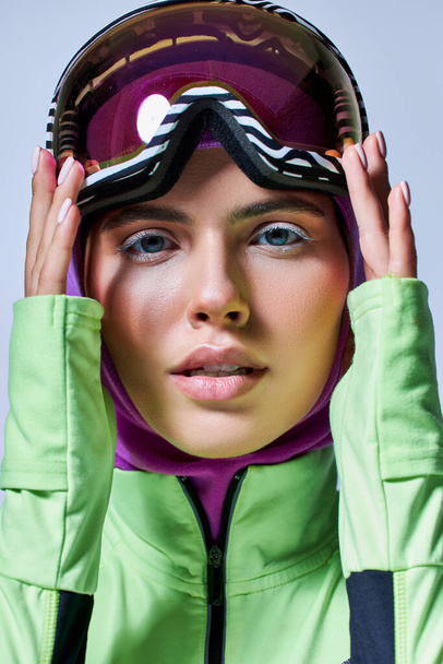 ładna kobieta w zimie aktywny strój z kominiarka na głowie regulacji okulary narciarskie na szarym tle - Zdjęcie, obraz