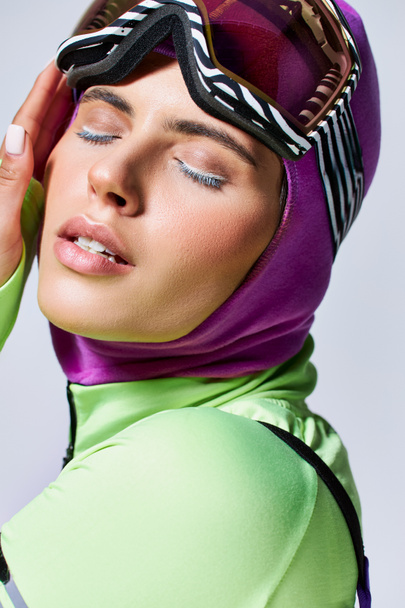 close up portrait of woman in winter ski clothes with balaclava on head touching face on grey - Fotoğraf, Görsel