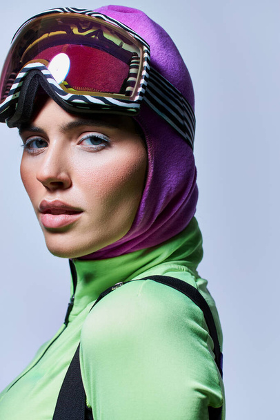 ritratto di donna in abiti da sci con passamontagna sulla testa guardando la macchina fotografica su grigio, trucco invernale - Foto, immagini