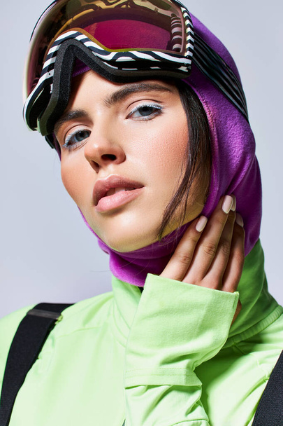 ritratto di donna in abiti da sci con passamontagna che guarda la macchina fotografica su grigio, modello con gli occhi azzurri - Foto, immagini