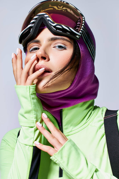 πορτρέτο της γυναίκας σε ρούχα σκι με balaclava θέτει σε γκρι φόντο, μοντέλο με μπλε μάτια - Φωτογραφία, εικόνα
