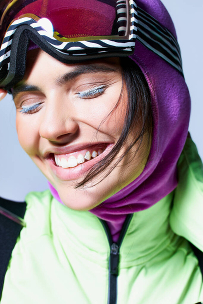 close up de mulher alegre no desgaste ativo com balaclava na cabeça sorrindo no fundo cinza - Foto, Imagem