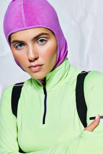 portrait of attractive woman with blue eyes posing in warm ski mask and active wear on grey backdrop - Photo, Image