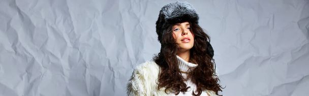 nádherná žena v bílé kožešinové bundě, zimní klobouk a svetr pózující na šedém pozadí, prapor - Fotografie, Obrázek