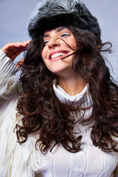 χαρούμενη γυναίκα σε λευκό faux γούνα σακάκι, καπέλο και πουλόβερ ποζάρουν σε γκρι φόντο, χειμώνα μόδας - Φωτογραφία, εικόνα
