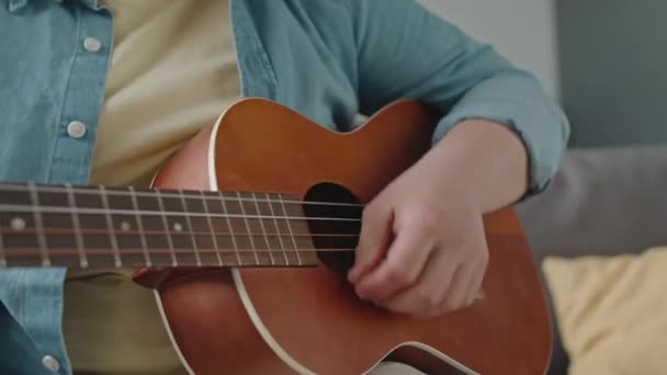 Inclinazione di una ragazza con la sindrome di Down seduta sul divano a casa e che suona musica con la chitarra - Filmati, video