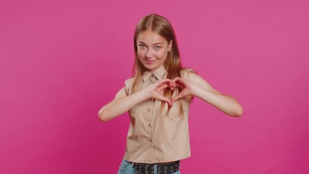 愛する女性. 笑顔の魅力的な女性は,ハートジェスチャーは,愛のサインが良い肯定的な感情と同情を表現することを示しています. ピンクのスタジオの壁の背景に孤立したかなり金髪の若い少女 - 映像、動画