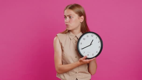 Woman with anxiety checking time on clock, running late to work, being in delay, deadline. Blonde busy girl looking at hour, minutes, worrying to be punctual isolated on pink studio background - Footage, Video
