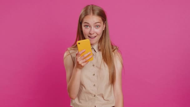 Νεαρή γυναίκα που αναζητούν smartphone οθόνη ειλικρινά χαρά νίκη, λαμβάνοντας χρήματα δολάρια μετρητά χαρτονομίσματα, γιορτάζει την επιτυχία τύχη λαχειοφόρων αγορών. Κορίτσι απομονωμένο σε ροζ φόντο στούντιο. Τρόπος ζωής - Πλάνα, βίντεο