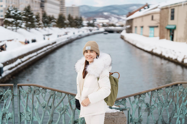小樽を訪れる女性観光客、冬は雪の小樽運河で幸せ旅行。北海道の観光スポットとして人気のランドマーク。旅行と休暇のコンセプト - 写真・画像