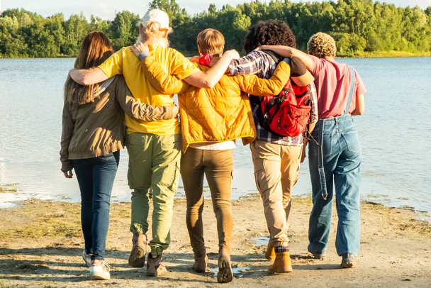 Koe vaeltava elämäntapa monipuolisena nuorten ystävien ryhmänä, joka syleilee luontoa, seisoo yhdessä metsäjärven rannalla. Ystävyys ja seikkailu esillä. Kaverit halailevat Forest Laken luona. Korkea - Valokuva, kuva
