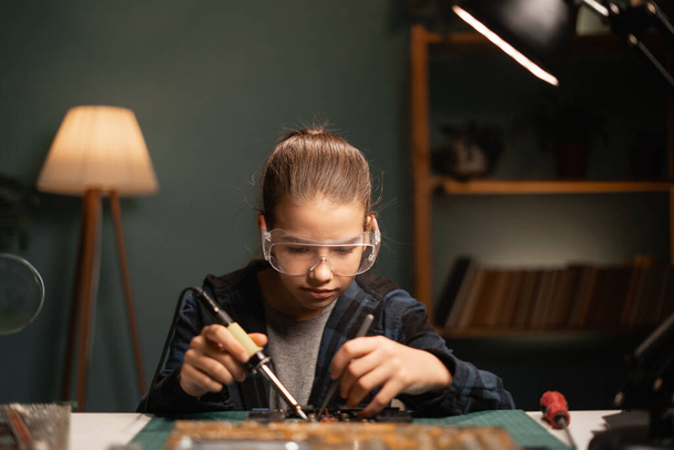 Умная школьница изучает электронику, паяльные провода и платы. Подросток работает над роботом в своей комнате. Копирование пространства - Фото, изображение