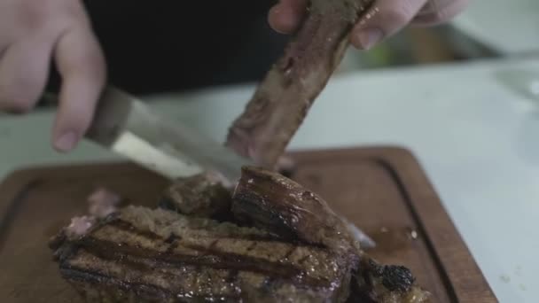 De chef snijdt stukken gekookt vlees op een snijplank met een mes. Trage beweging, close-up. - Video