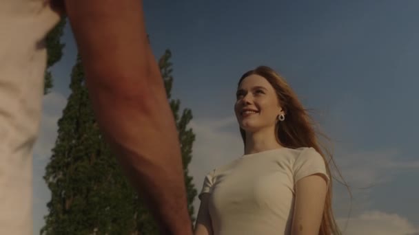 Red headed woman and a handsome man are holding hands and looking at each other, standing in the middle of rural nature. Outdoor lifestyle portrait - Footage, Video