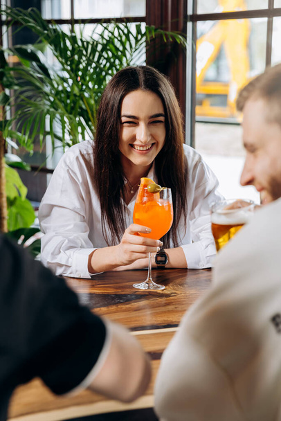 Junge lächelnde Frau genießt einen Coctail in Bar-Restaurant während der Erholung mit Freunden - Foto, Bild