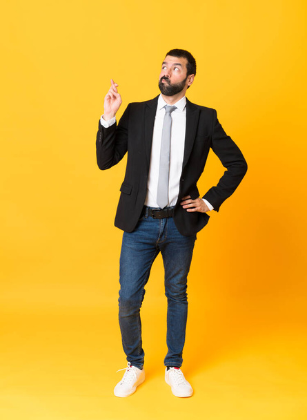Full-length shot van zakenman over geïsoleerde gele achtergrond met vingers kruisen en wensen de beste - Foto, afbeelding