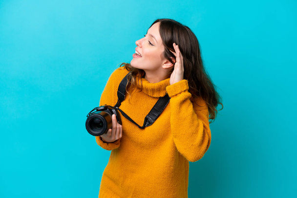 Nuori valokuvaaja nainen eristetty sinisellä taustalla kuuntelemalla jotain laittamalla käsi korvaan - Valokuva, kuva